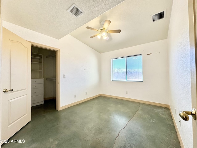 unfurnished bedroom with visible vents, a textured ceiling, a walk in closet, and vaulted ceiling