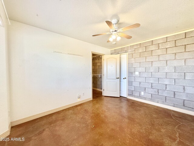 empty room with a textured ceiling, finished concrete flooring, baseboards, and a ceiling fan