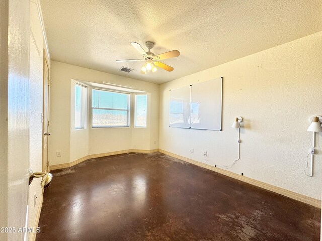 unfurnished room with ceiling fan, finished concrete flooring, baseboards, and a textured ceiling