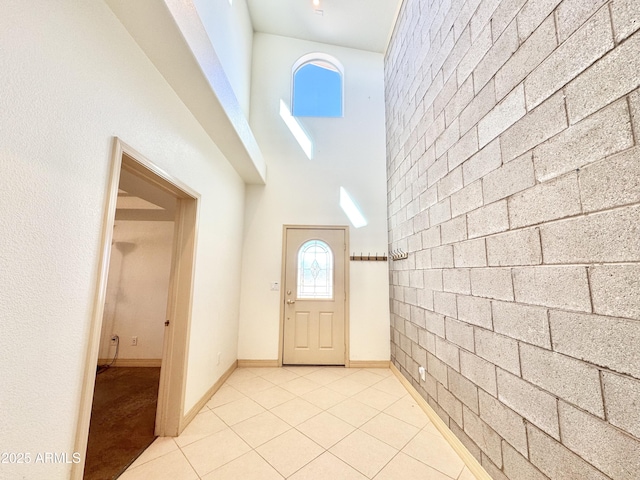 foyer entrance with brick wall, light tile patterned floors, baseboards, and a towering ceiling