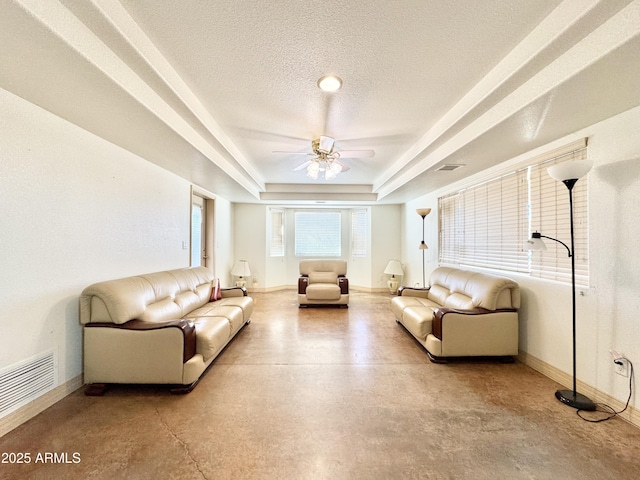 living room with a tray ceiling, visible vents, baseboards, and a textured ceiling