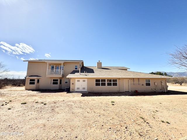 rear view of house featuring stucco siding, french doors, a balcony, central AC unit, and a chimney