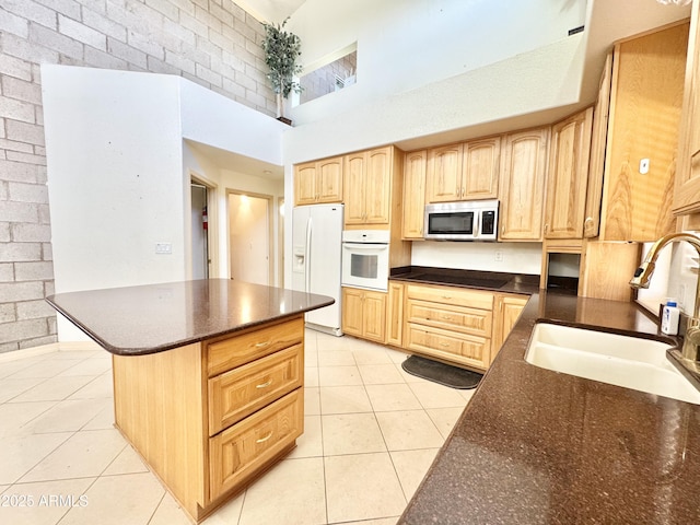 kitchen featuring light brown cabinetry, a sink, white appliances, a high ceiling, and light tile patterned flooring