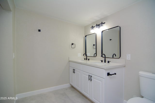 bathroom with toilet, double vanity, baseboards, and a sink