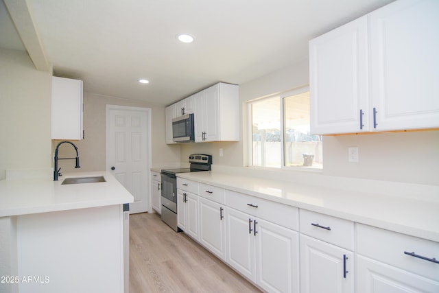 kitchen featuring recessed lighting, light wood-style flooring, appliances with stainless steel finishes, white cabinetry, and a sink