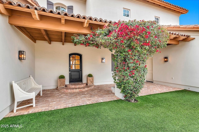 view of exterior entry with stucco siding, a yard, and a tiled roof