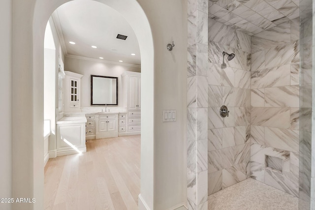 full bath featuring a tile shower, vanity, crown molding, and wood finished floors