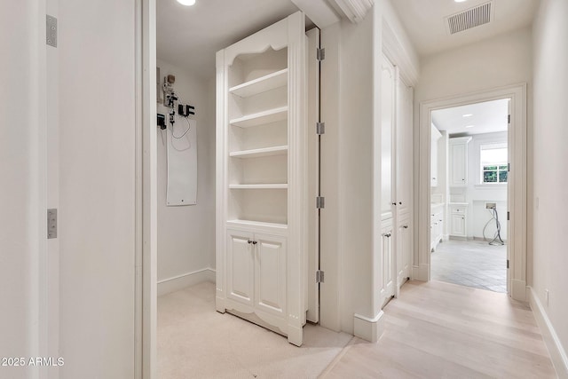 corridor featuring light wood-style floors, baseboards, and visible vents