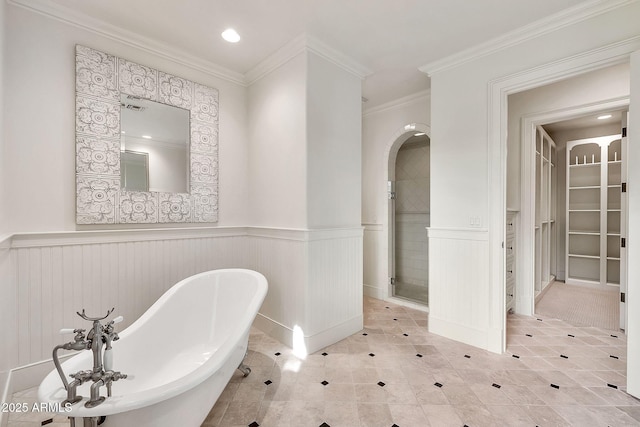 bathroom with crown molding, a walk in closet, a wainscoted wall, a freestanding bath, and a stall shower