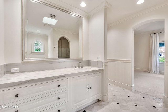 bathroom with vanity, a wainscoted wall, visible vents, a skylight, and crown molding