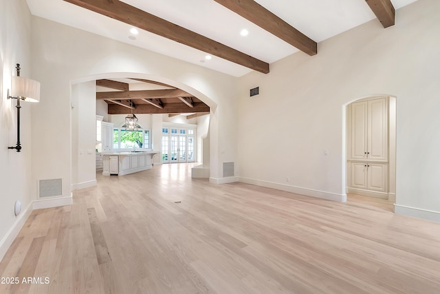 empty room featuring arched walkways, visible vents, light wood finished floors, and baseboards