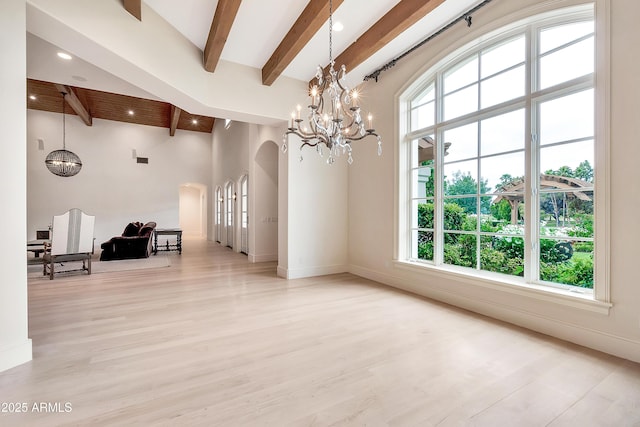 interior space with beamed ceiling, light wood-type flooring, a high ceiling, an inviting chandelier, and arched walkways