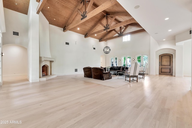living area featuring visible vents, beam ceiling, arched walkways, light wood-style floors, and wooden ceiling