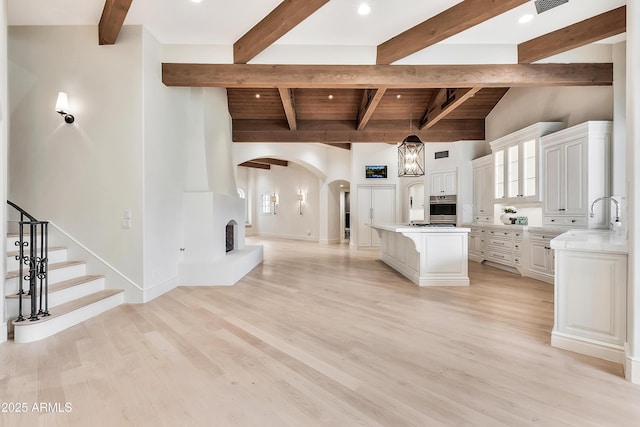 kitchen with light wood-style flooring, lofted ceiling with beams, a center island, white cabinetry, and arched walkways