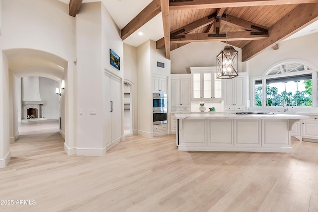 kitchen with high vaulted ceiling, light wood-style flooring, a center island, white cabinetry, and a chandelier