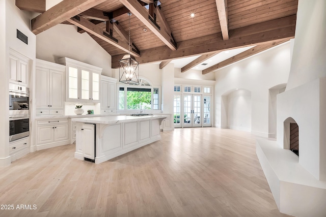 kitchen featuring visible vents, a center island, high vaulted ceiling, light wood-type flooring, and white cabinetry