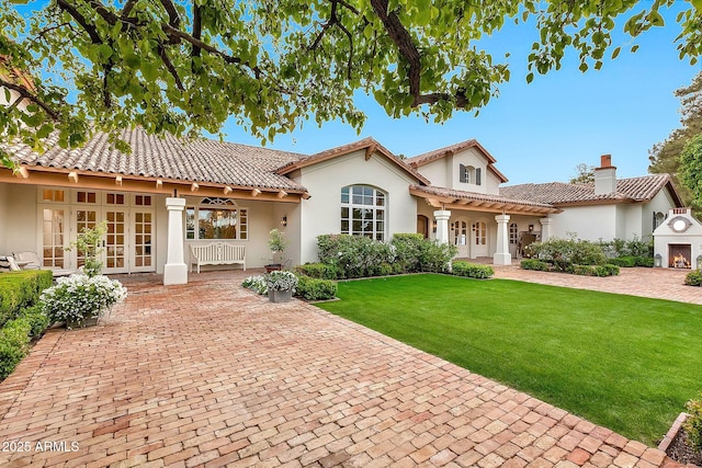 mediterranean / spanish house with stucco siding, a tile roof, french doors, a front yard, and a chimney
