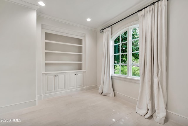spare room with built in shelves, light wood-type flooring, baseboards, and ornamental molding