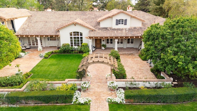 back of property featuring stucco siding, a tiled roof, a chimney, and a yard