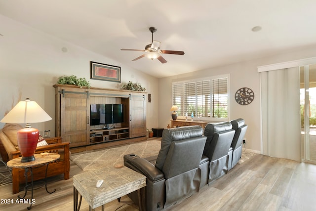 living room featuring lofted ceiling, light hardwood / wood-style floors, a barn door, and ceiling fan