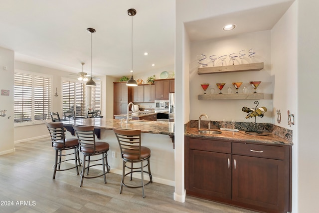 kitchen featuring dark stone counters, ceiling fan, hanging light fixtures, sink, and light hardwood / wood-style floors