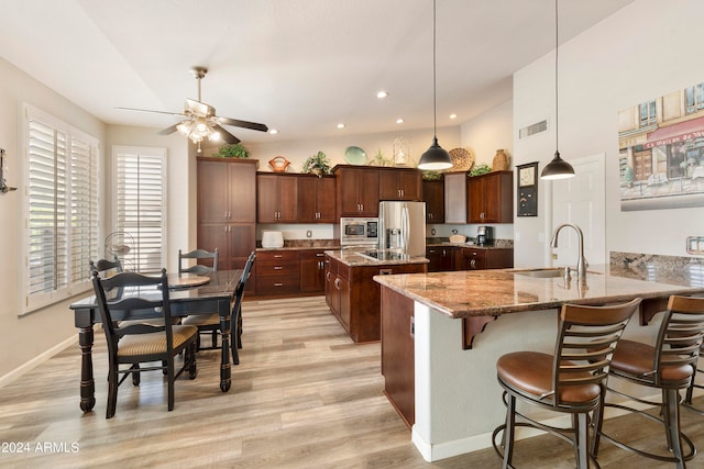 kitchen featuring stainless steel appliances, light hardwood / wood-style floors, light stone counters, and a center island with sink