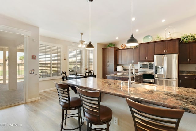 kitchen featuring decorative light fixtures, light wood-type flooring, sink, light stone counters, and appliances with stainless steel finishes