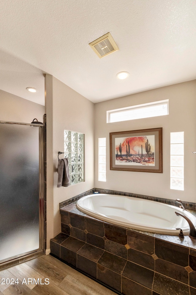 bathroom with a textured ceiling, separate shower and tub, wood-type flooring, and plenty of natural light