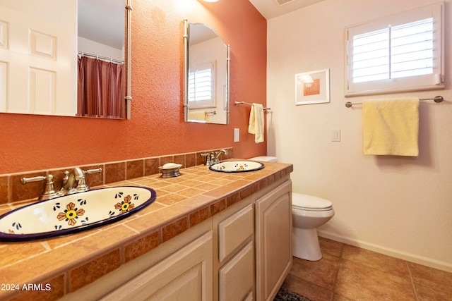 bathroom with dual vanity, toilet, a wealth of natural light, and tile patterned flooring