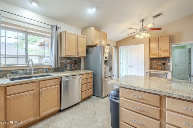 kitchen with light brown cabinets, a sink, vaulted ceiling, appliances with stainless steel finishes, and backsplash