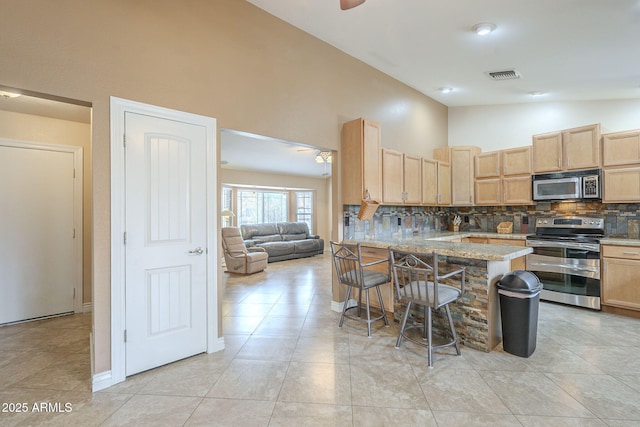 kitchen with light brown cabinets, stainless steel appliances, visible vents, backsplash, and a kitchen bar