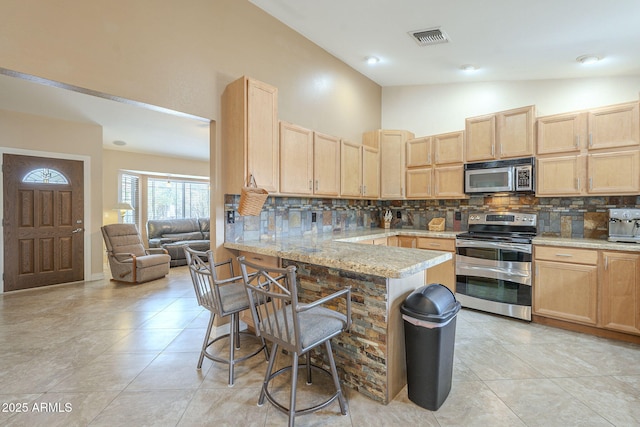 kitchen with visible vents, decorative backsplash, appliances with stainless steel finishes, a kitchen breakfast bar, and light brown cabinets