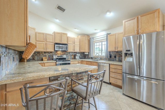 kitchen featuring lofted ceiling, light brown cabinetry, appliances with stainless steel finishes, light tile patterned flooring, and a peninsula