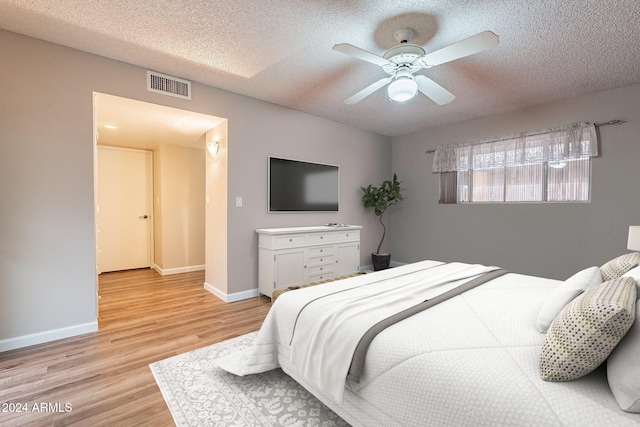 bedroom with ceiling fan, light wood-type flooring, and a textured ceiling