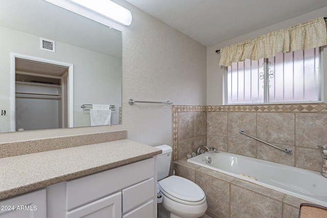 bathroom with vanity, tiled bath, and toilet