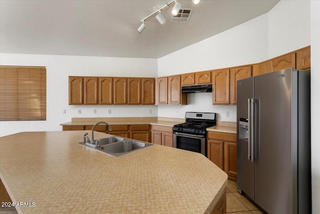 kitchen with a center island with sink, rail lighting, sink, light tile patterned flooring, and stainless steel appliances