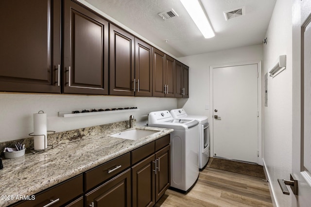 clothes washing area featuring independent washer and dryer, cabinets, sink, and light wood-type flooring