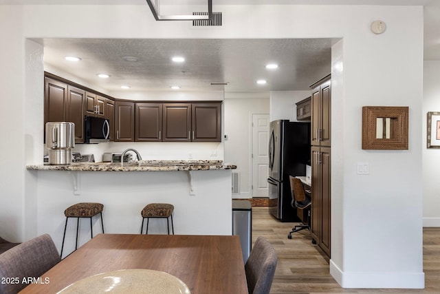 kitchen with a breakfast bar area, black fridge, light hardwood / wood-style flooring, kitchen peninsula, and light stone countertops