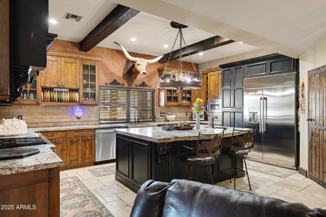 21230 S 156th St, Gilbert, AZ 85298 - kitchen with built in appliances, stone tile flooring, beamed ceiling, tasteful backsplash, and an island with sink