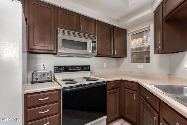 kitchen with white appliances, dark brown cabinetry, and light tile patterned floors