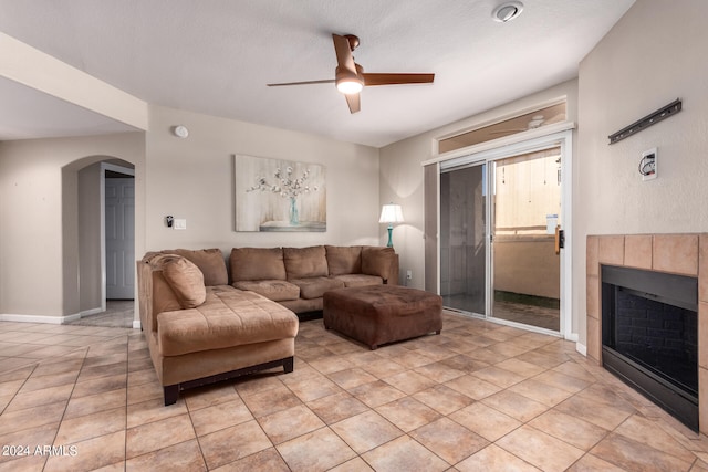 living room with ceiling fan, a textured ceiling, light tile patterned flooring, and a tile fireplace