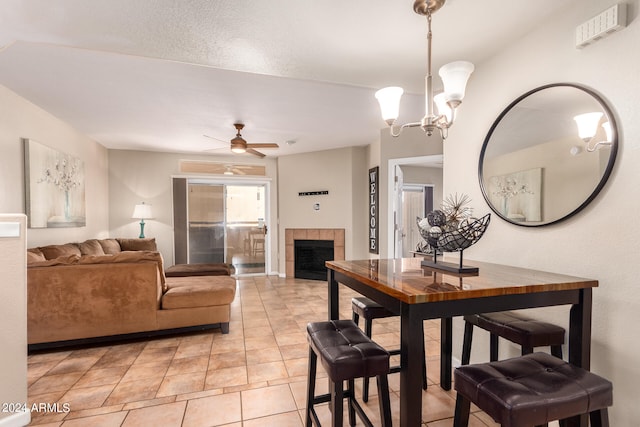 dining room with ceiling fan with notable chandelier, a tile fireplace, and light tile patterned floors