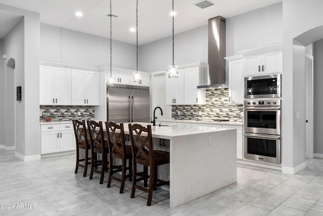 kitchen featuring built in appliances, white cabinets, wall chimney exhaust hood, a kitchen island with sink, and a high ceiling