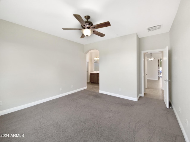 unfurnished bedroom with ceiling fan, ensuite bathroom, and dark colored carpet