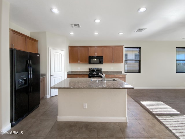 kitchen featuring black appliances, light stone counters, sink, and a kitchen island with sink