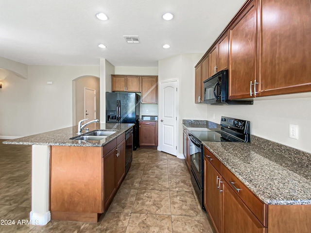 kitchen featuring sink, a kitchen island with sink, dark stone counters, and black appliances