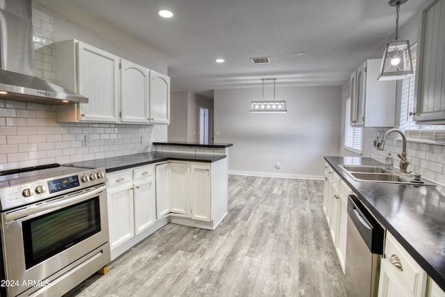 kitchen with pendant lighting, wall chimney range hood, light wood-type flooring, and stainless steel appliances