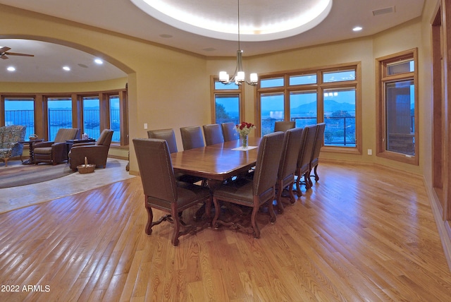 dining room with ceiling fan with notable chandelier, a mountain view, light wood-type flooring, and a tray ceiling