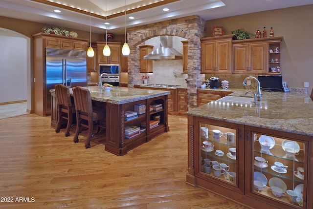 kitchen with sink, wall chimney exhaust hood, built in appliances, kitchen peninsula, and pendant lighting