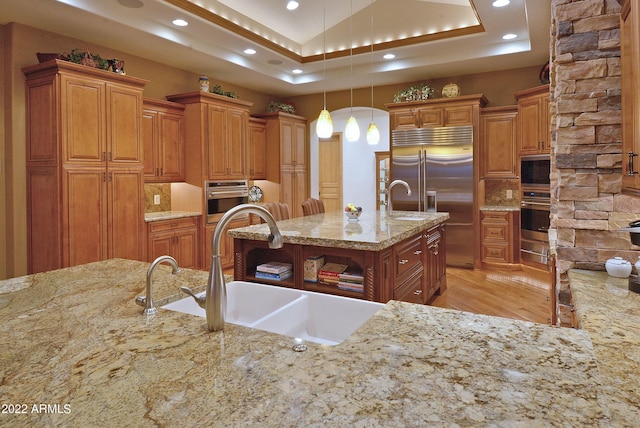 kitchen with light stone countertops, sink, built in appliances, decorative light fixtures, and decorative backsplash